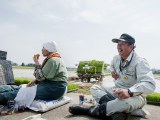 農道に置いた肥料袋に腰掛けて、３時のお茶をする安念則夫さん（右）と母の玲子さん